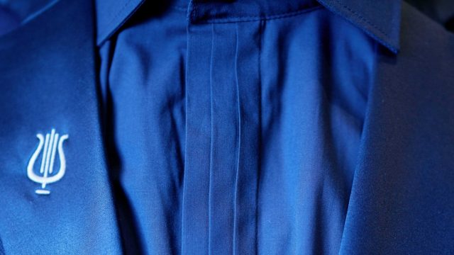 De plooien op het overhemd zijn geïnspireerd op de drie lijnen van de gouden lier op het dak